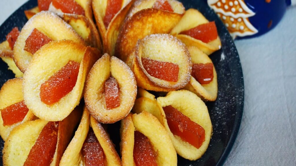 Many calla flower cookies with red jelly arranged on a plate and dusted with powdered sugar.