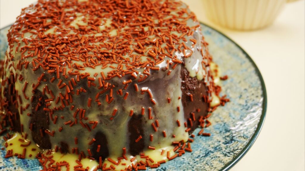 Chocolate flan on a plate, covered with white chocolate sauce and chocolate sprinkles.