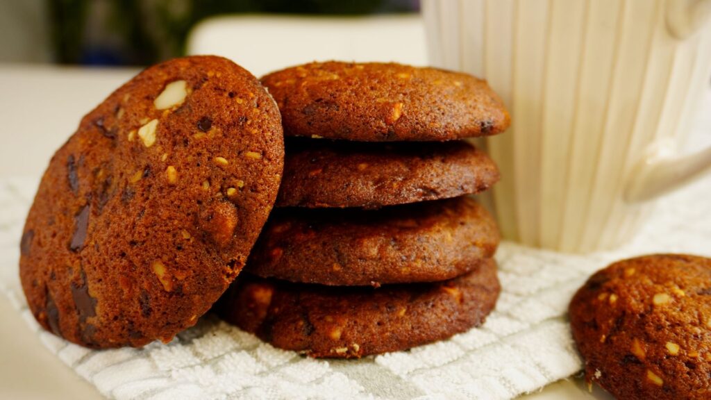 Four coffee cookies stacked one on another by a white mug. Another cookie placed sideways next to the four.