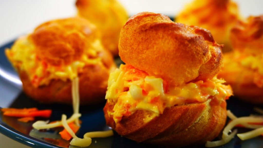 Freshly baked cream puffs with cheese salad filling on a dark blue plate.