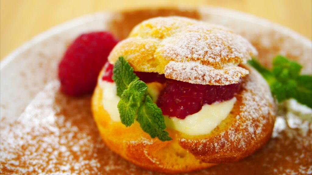 Freshly baked cream puff with whipped cream filling on a plate. Decorated with raspberries, mint leaves and powdered sugar.