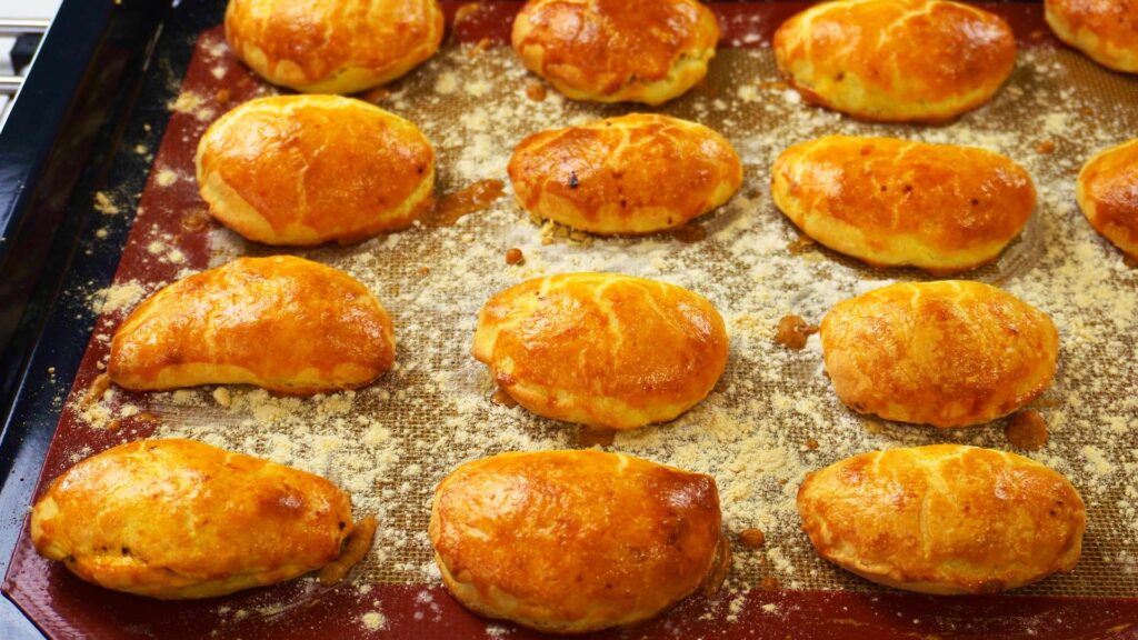 12 small meat pies on a baking tray fresh from the oven.