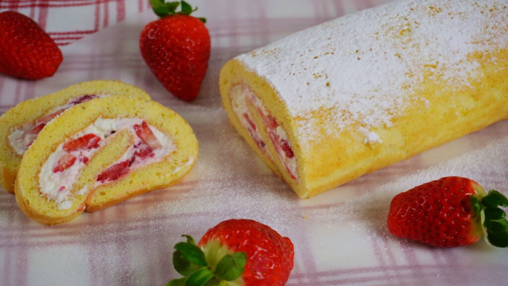 Strawberry Swiss roll cake with two slices cut on a piece of parchment paper with several strawberries around.